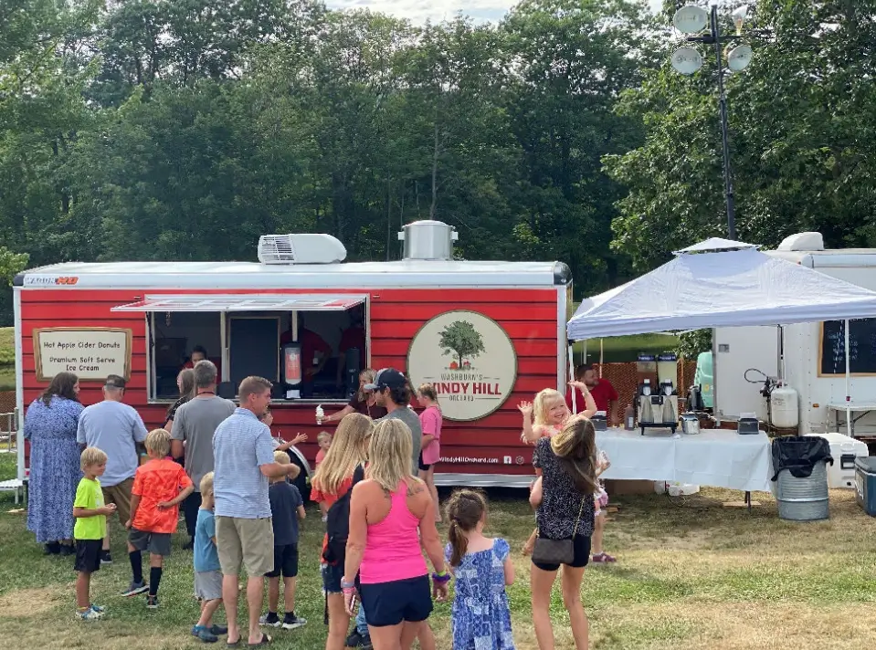 A food trailer with lots of people buying food with their kids.