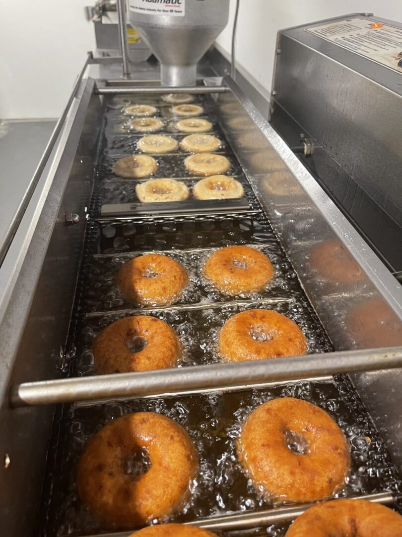 Donuts frying in hot oil on a conveyor belt.